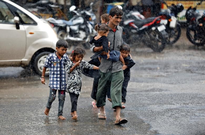 A man carrying children crosses a road during heavy rains in Ahmedabad, India. REUTERS/Amit Dave